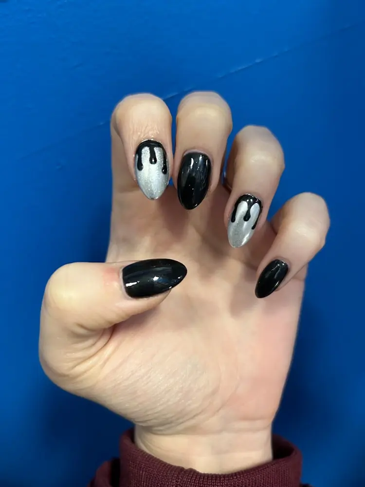 Black and silver almond nails with a dripping design, on a blue backdrop