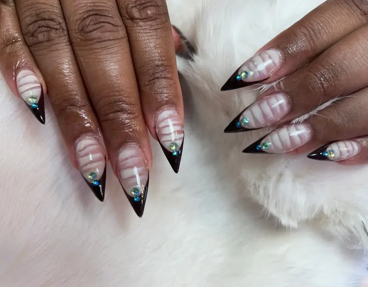 Long almond nails fading from sheer nude into black tips, resting on white fur