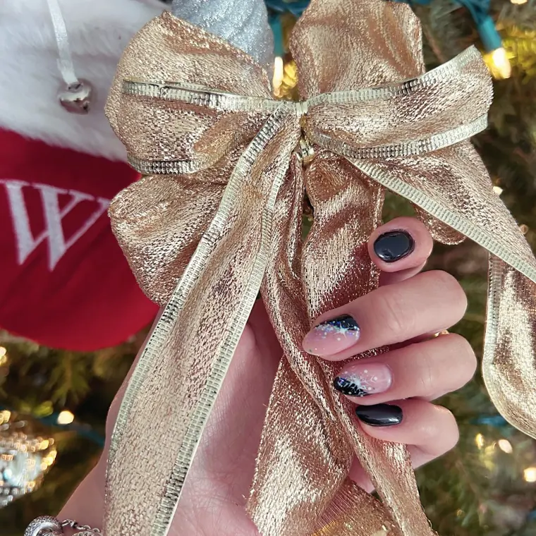Short nails in black and sheer pink with small sparkle details, held beside a gold bow