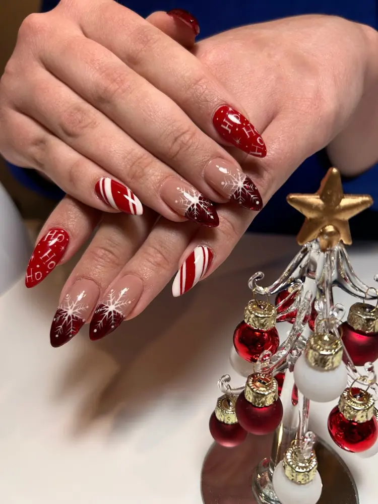 Red almond nails with white candy-cane stripes beside a tiny Christmas tree
