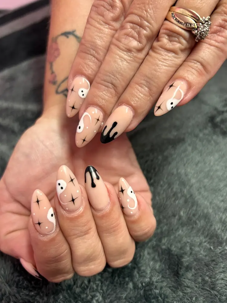 Almond nails in soft nude with tiny black and white ghost faces and small sparkles