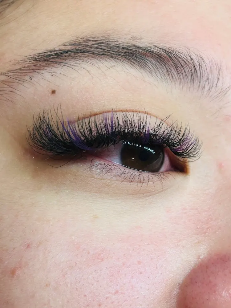 Close-up of an eye with full, curled lash extensions and a few purple strands