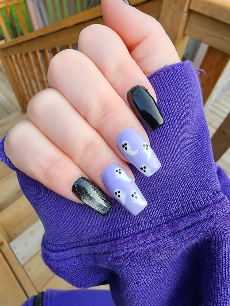 Long square nails in lilac with white ghosts, plus two glossy black nails, against a purple sleeve