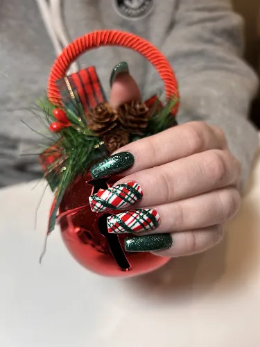 Red, green and black tartan plaid nails held against a glass ornament